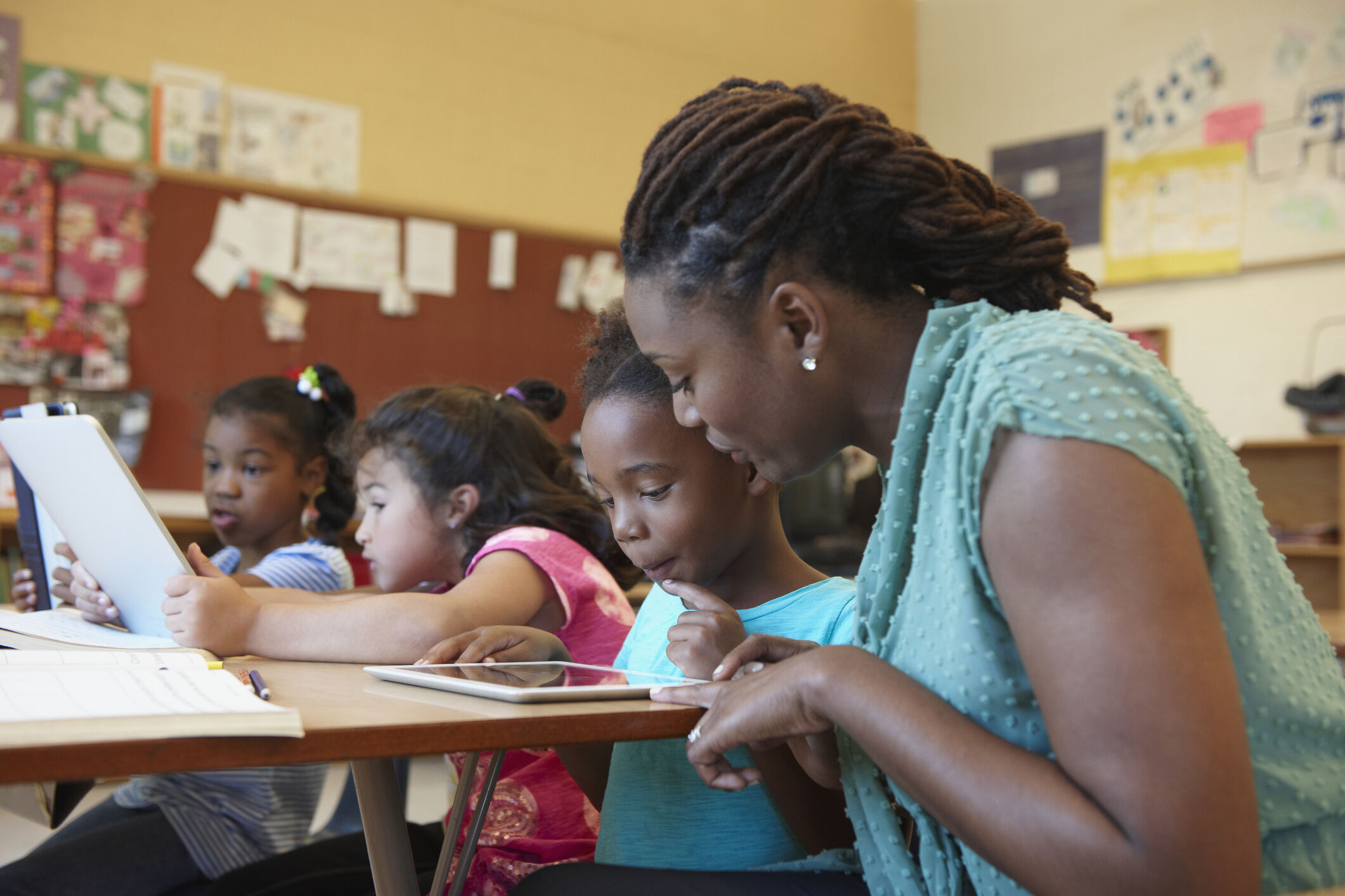 Young teacher in classroom helping a student at her desk